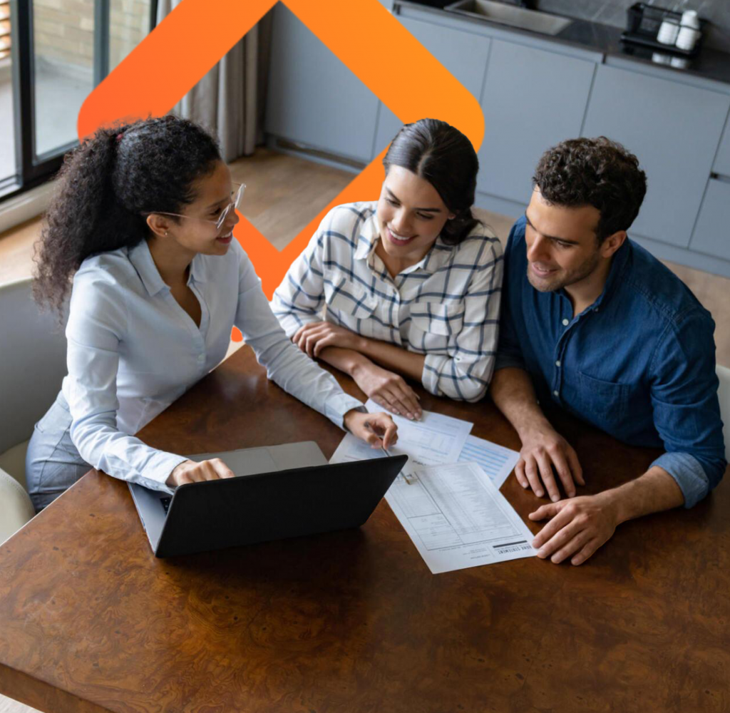 Three people discuss business documents at a table with a laptop.